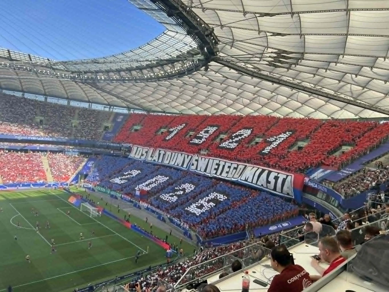 Oprawa Rakowa Częstochowa trybuny stadionu wypełnione kibicami trzymającymi kartony tworzące efektowną choreografię w barwach czerwonej i niebieskiej, układającą się w napis '1946' na górze i '2024' na dole, a po środku transparent z napisem '105 LAT DUMNY ŚWIĘTEGO MIASTA', na ...