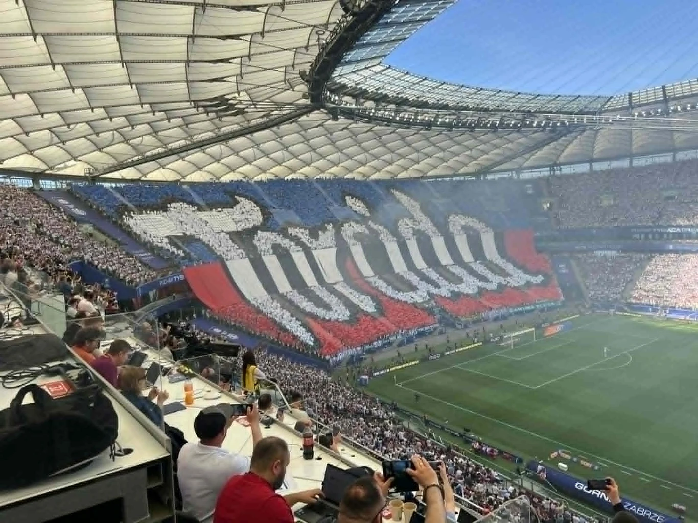 Oprawa Górnika Zabrze tłum kibiców tworzący spektakularną kartoniadę w barwach biało-czerwono-niebieskich z ogromnym napisem „Torcida” na trybunach dużego stadionu podczas meczu piłkarskiego