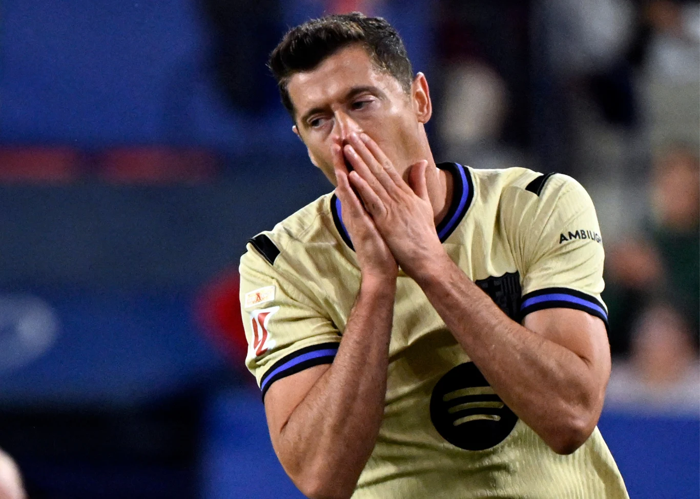 Robert Lewandowski w meczu Osasuna - FC Barcelona piłkarz w jasnej koszulce z logo Spotify obejmuje dłońmi twarz, wyrażając rozczarowanie lub smutek, tło rozmyte z widocznymi innymi osobami