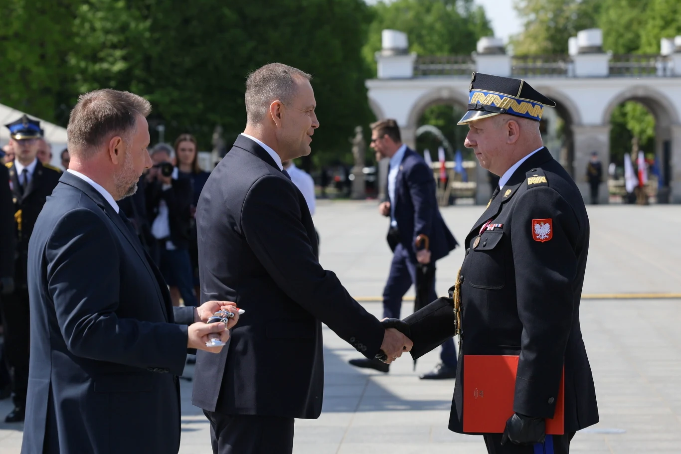 Karol Nawrocki, Marcin Kierwiński oraz awansowany na stopień nadbrygadiera zastępca komendanta głównego PSP Sławomir Sierpatowski Uścisk dłoni Karola Nawrockiego i Sławomira Sierpatowskiego podczas wręczenia awansu generalskiego, w tle Grób Nieznanego Żołnierza.