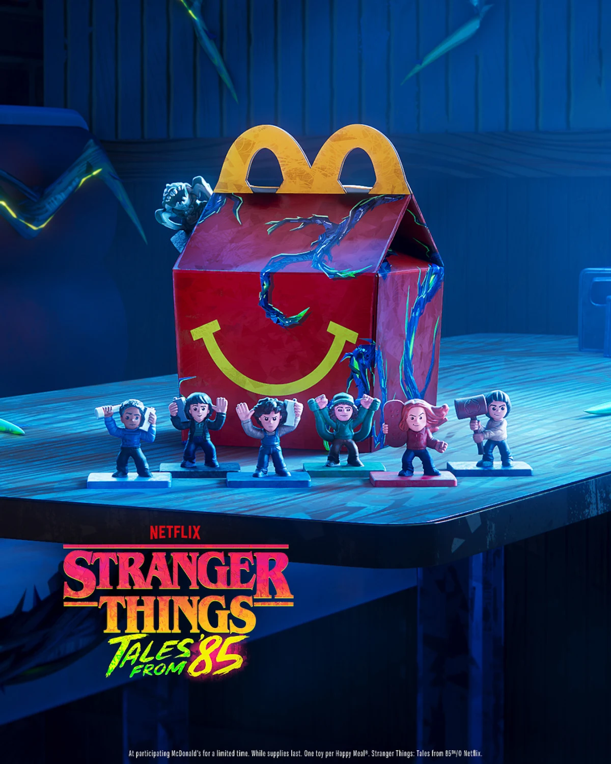 Nowy Happy Meal z zestawem gadżetów nawiązujących do nowej animacji z kultowej serii Netflixa "Stranger Things: Opowieści z '85" Skrzynka Happy Meal z charakterystycznym żółtym uśmiechem oraz figurki postaci z serialu Stranger Things ustawione przed nią na stole.