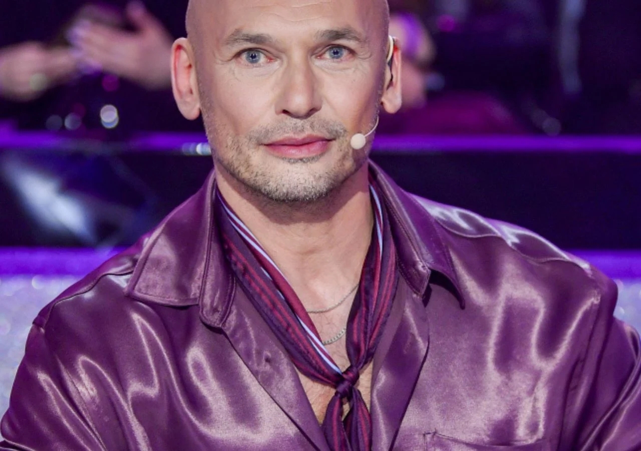 Tomasz Wygoda w programie "Taniec z gwiazdami" Tomasz Wygoda, juror programu "Taniec z gwiazdami", w połyskującej fioletowej koszuli i kolorowej apaszce.