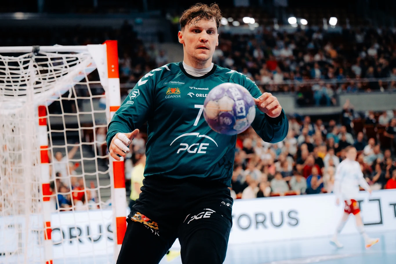 PGE Wybrzeże Gdańsk – ORLEN Wisła Płock Bramkarz w stroju sportowym łapie piłkę ręczną na tle bramki i licznie zgromadzonej publiczności na trybunach.