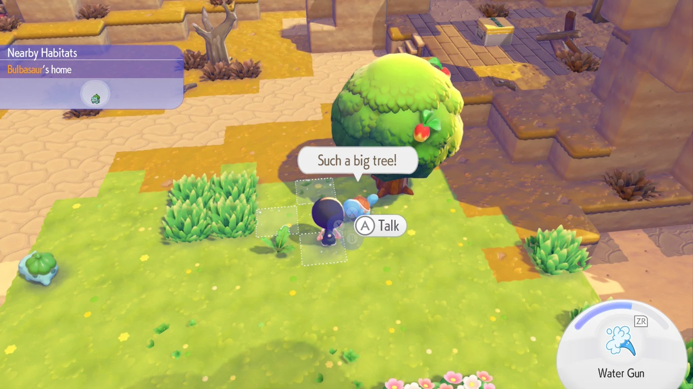 Postać z niebieskim pokemonem rozmawia przy dużym drzewie owocowym na tle trawiastej polany z fragmentami piasku i kamiennych schodów.