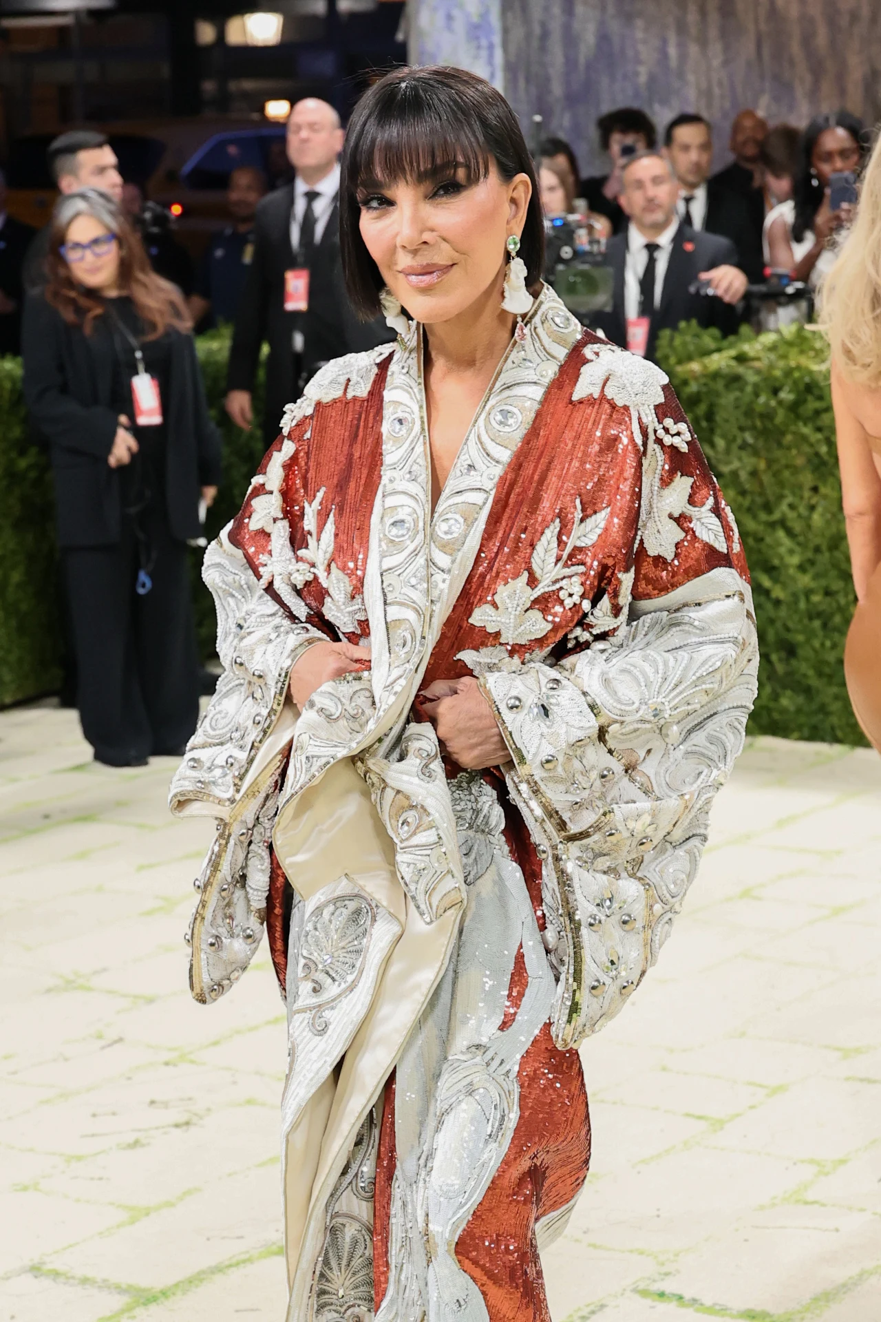 Przez ostatnie tygodnie internet huczał od plotek na temat twarzy Kris Jenner Kobieta w eleganckiej, ozdobnej kreacji w odcieniach bieli i czerwieni z bogatymi haftami, stojąca na wydarzeniu z obecnością fotoreporterów i ochroniarzy w tle.