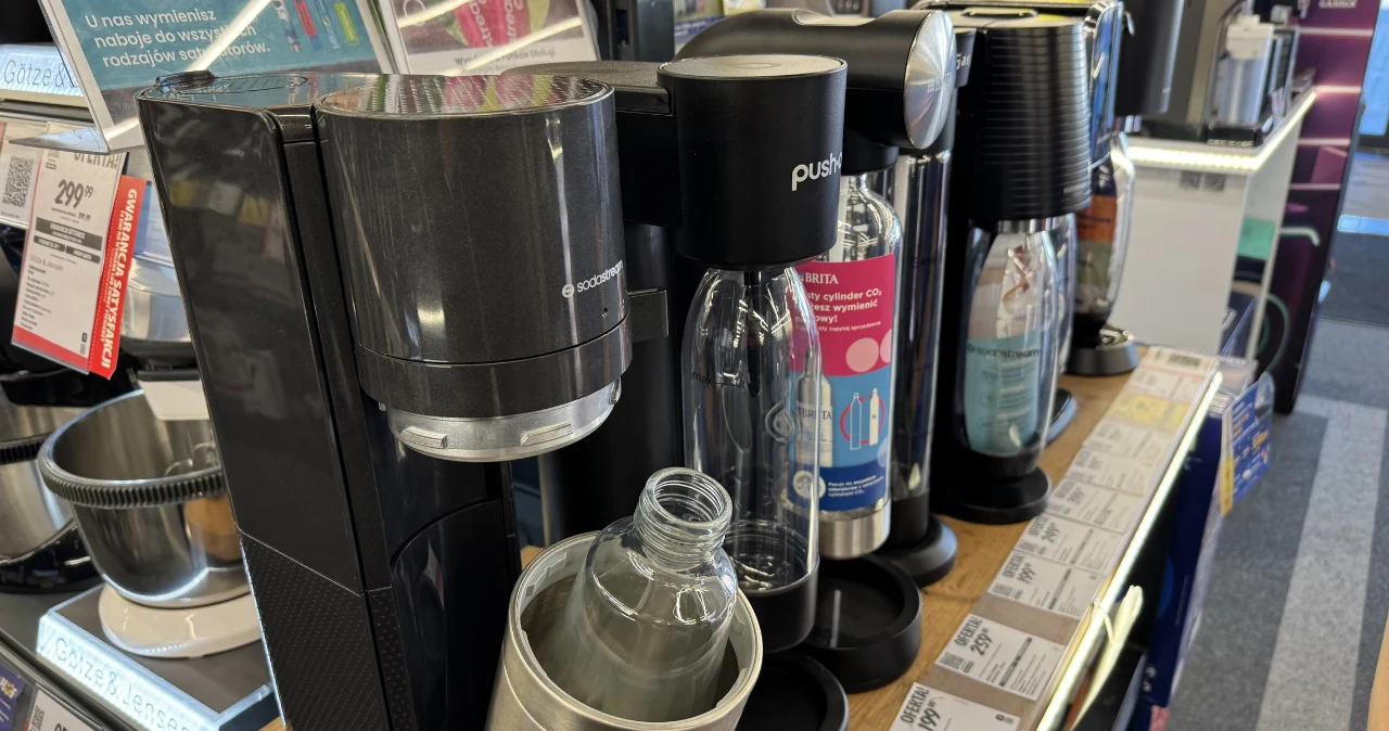 SodaStream 169,00 zł w Lidlu – ceny nabojów, wymiana i koszty użytkowania Ekspozycja saturatorów SodaStream z przezroczystymi butelkami i ceną na półce sklepowej.