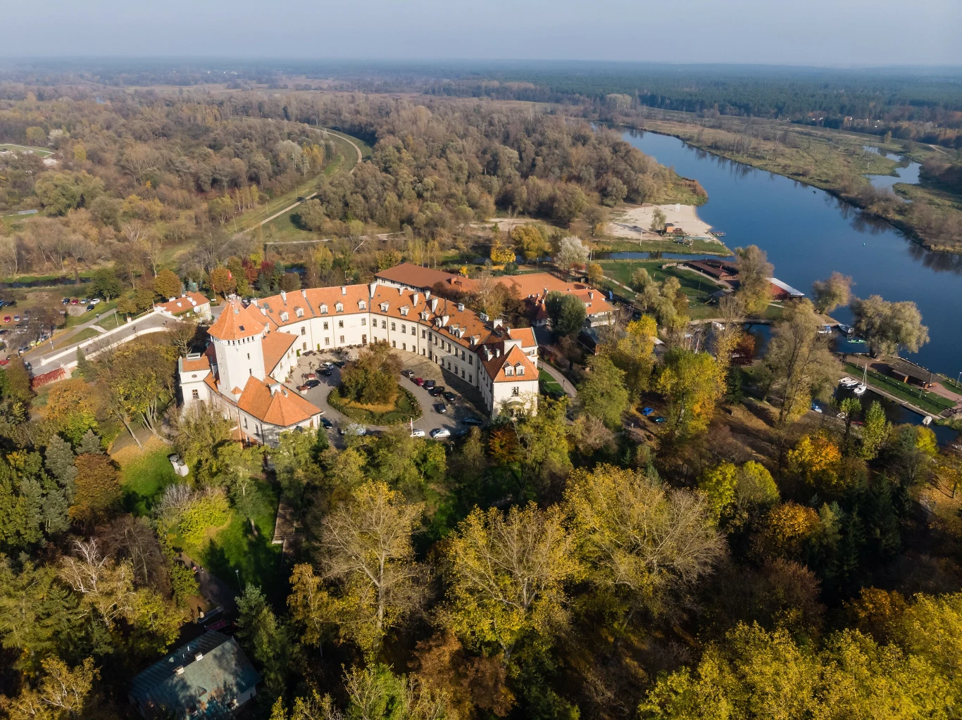 Dlaczego Pułtusk nazywany jest ”Wenecją Mazowsza”? Zamek z czerwonym dachem i białymi murami, otoczony zielenią, położony nad zakolem rzeki w Pułtusku.