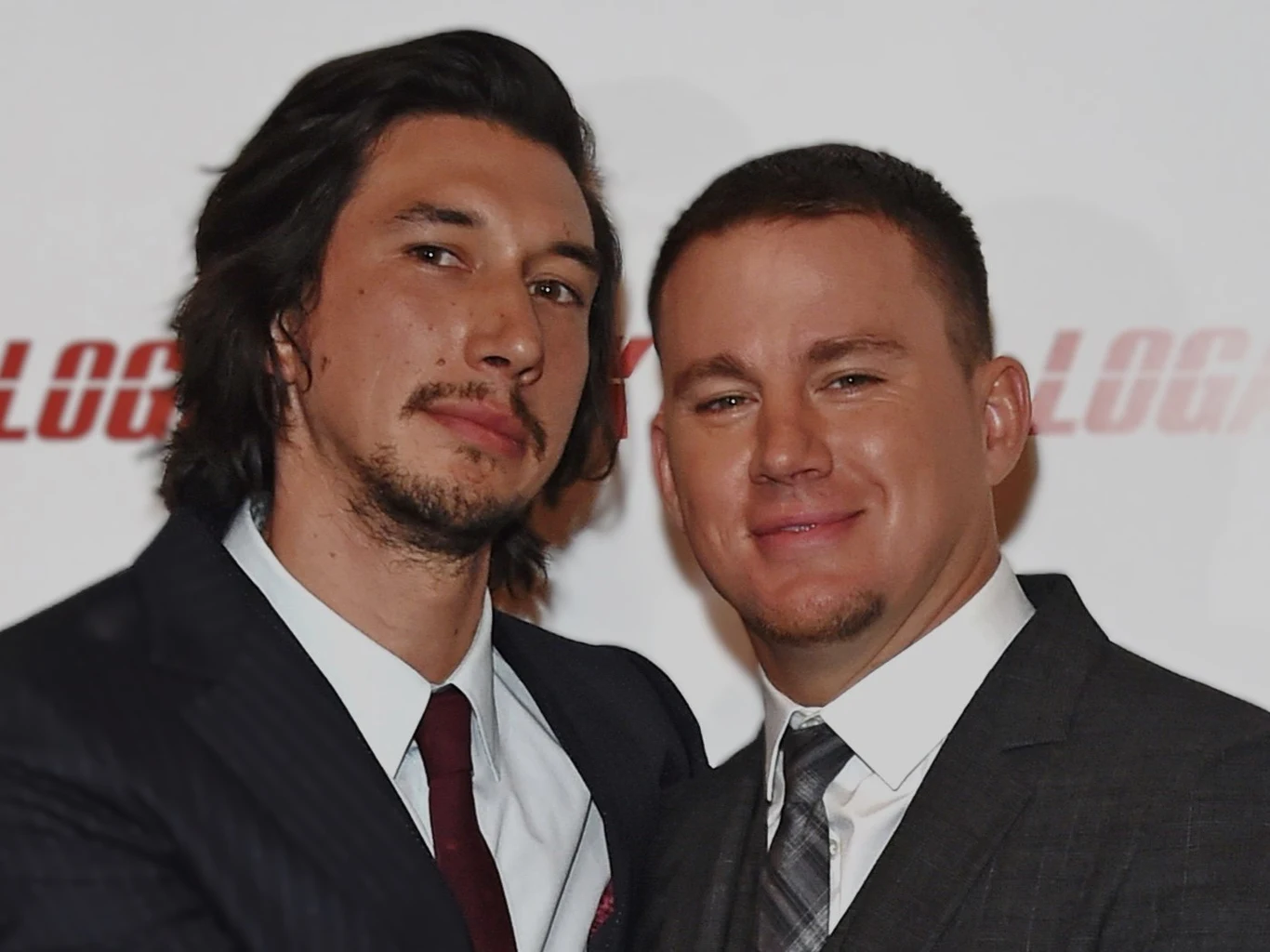 Adam Driver i Channing Tatum Dwóch mężczyzn w eleganckich garniturach pozuje razem do zdjęcia na tle jasnej ścianki z rozmytym napisem.