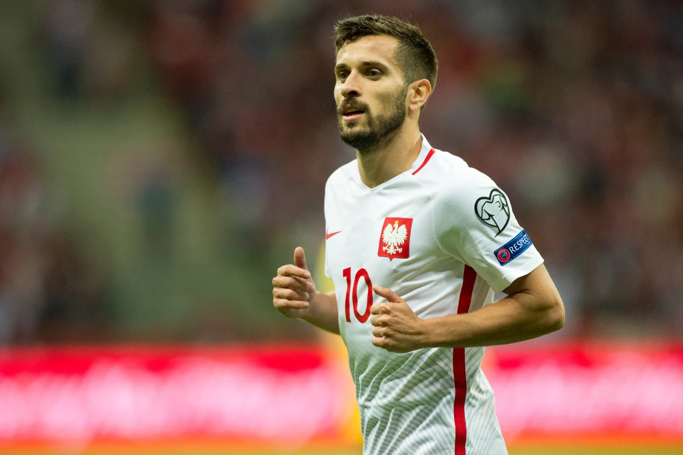 Maciej Makuszewski ma na koncie pięć występów w reprezentacji Polski Piłkarz w białej koszulce z orłem na piersi i numerem 10 podczas meczu piłkarskiego na stadionie.