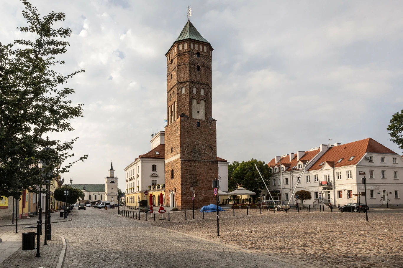 Najdłuższym brukowanym rynkiem w Europie jest rynek w Pułtusku Dominująca ceglana wieża z charakterystycznym hełmem otoczona brukowanym placem i niskimi zabudowaniami z czerwonymi dachami.