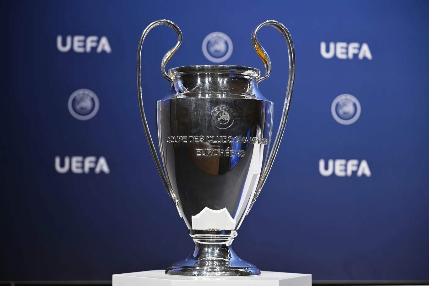 Charakterystyczny puchar z "uszami", który otrzyma zwycięzca Ligi Mistrzów 2026 Srebrny puchar Ligi Mistrzów UEFA z dużymi uszami na białym postumencie, w tle ścianka z logotypami UEFA.