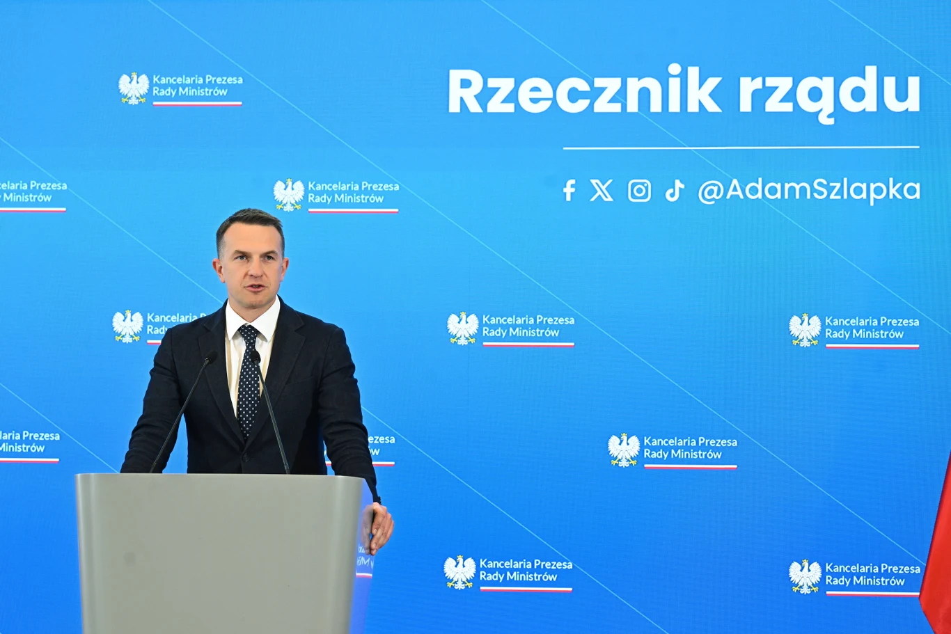 Rzecznik rządu Adam Szłapka podczas konferencji prasowej Adam Szłapka na konferencji prasowej, stoi za mównicą.