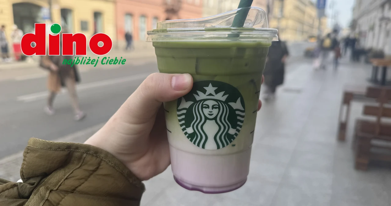 Dino wprowadza zimną kawę Starbucks. Do 12.05 promocja 2+1 Plastikowy kubek Starbucks z warstwowym napojem, trzymany na tle ulicy, logo Dino w rogu.