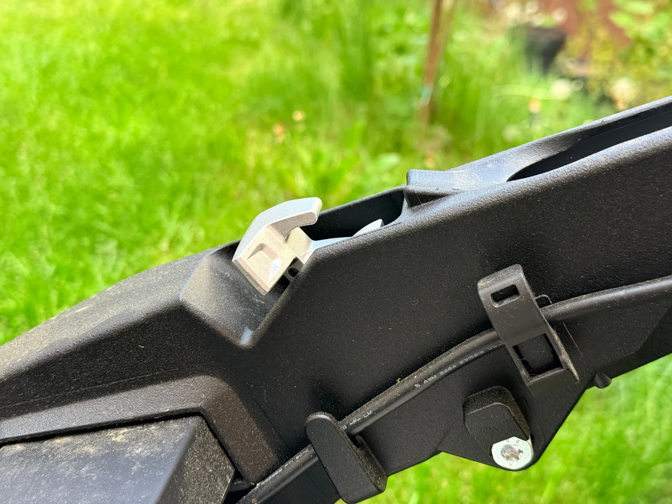 Wszystkie elementy są dobrze spasowane i wykonane z wysokiej jakości materiałów Zbliżenie na element mechanizmu roweru elektrycznego, widoczny plastikowy zaczep oraz fragment ramy z przewodem zabezpieczonym opaską.