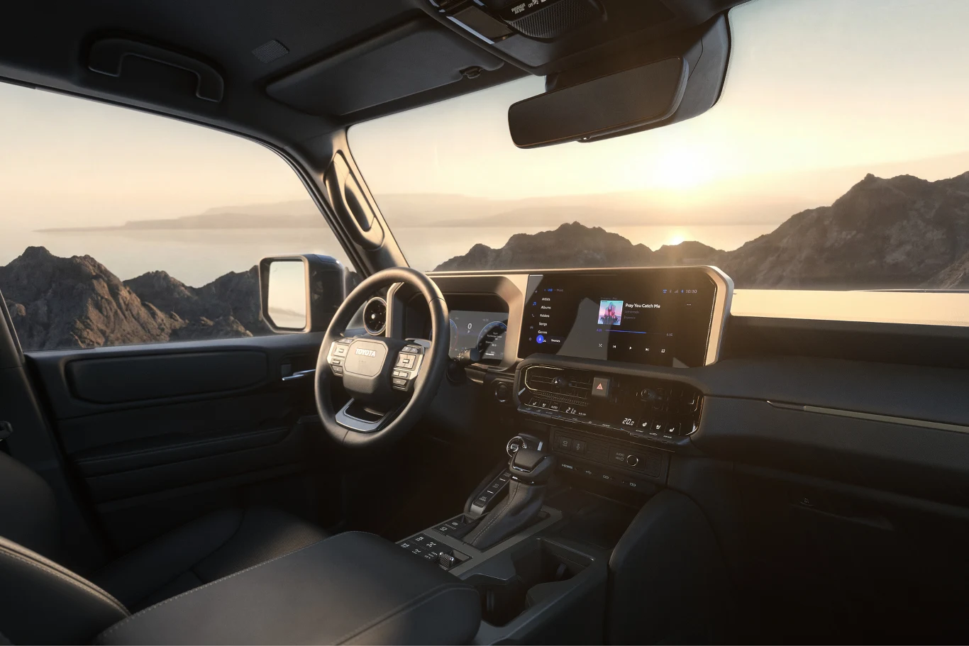 Wnętrze nowej Toyoty Land Cruiser. Nowoczesne wnętrze samochodu z dużym ekranem multimedialnym na desce rozdzielczej, skórzaną kierownicą i widokiem na górzysty krajobraz za szybą oświetlony promieniami zachodzącego słońca.