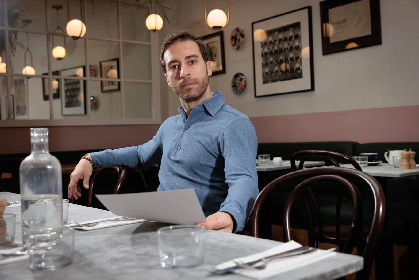 Mathieu Flamini Mathieu Flamini w niebieskiej koszuli siedzi przy stole w restauracji, trzyma kartkę papieru; puste talerze i woda.