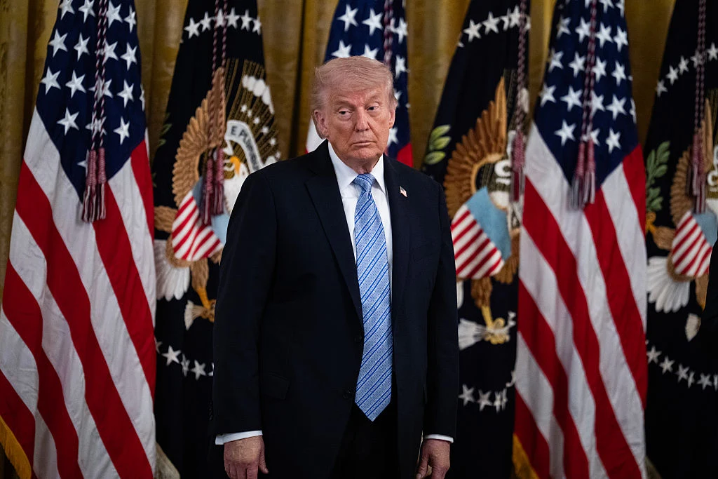 Taktyka Donalda Trumpa wobec Iranu nie sprawdza się Mężczyzna w garniturze i krawacie stoi na tle wielu amerykańskich flag oraz emblematów z herbem Stanów Zjednoczonych.