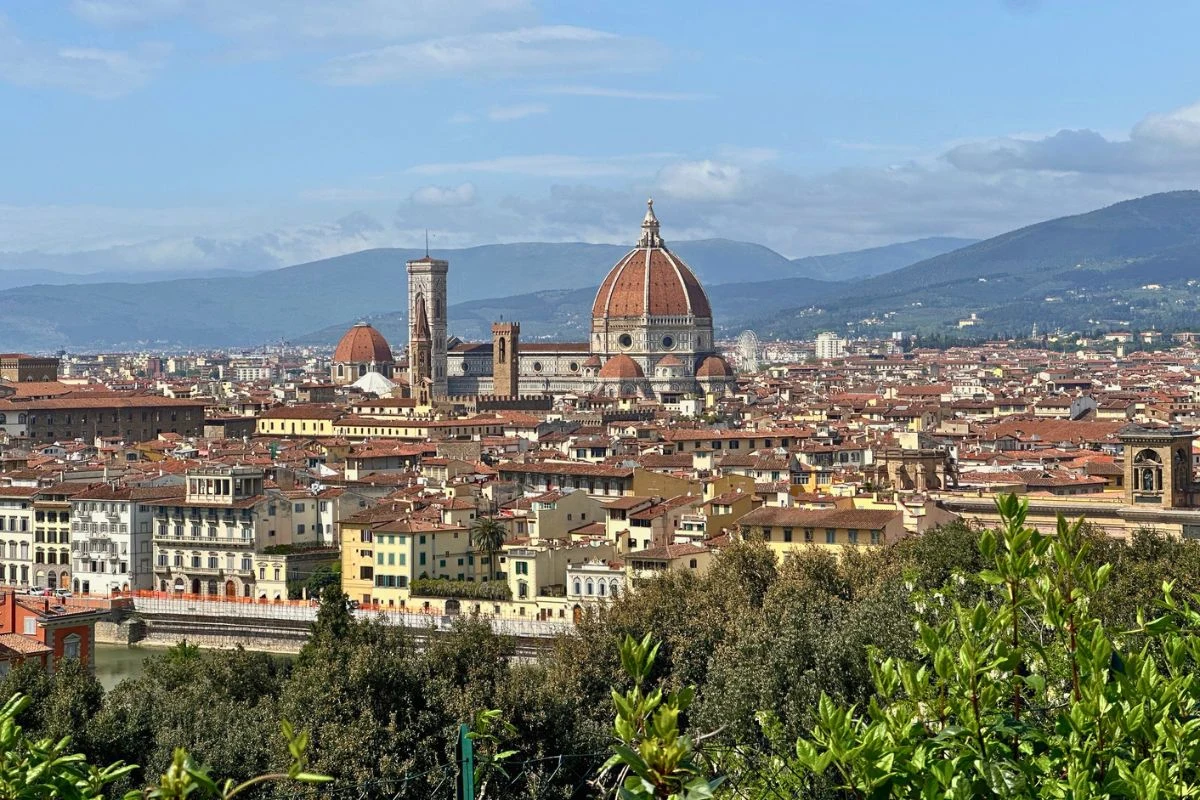 Panorama Florencji z dominującą katedrą Santa Maria del Fiore, widocznym czerwoną kopułą oraz otaczającą ją zabudową miasta, na tle górskich wzniesień.