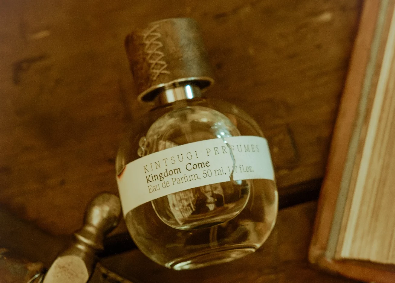 Perfumy z Kingdom Come będą hitem rynkowym? Flakon perfum Kintsugi Perfumes Kingdom Come z drewnianą zakrętką, umieszczony obok książki na drewnianej powierzchni.
