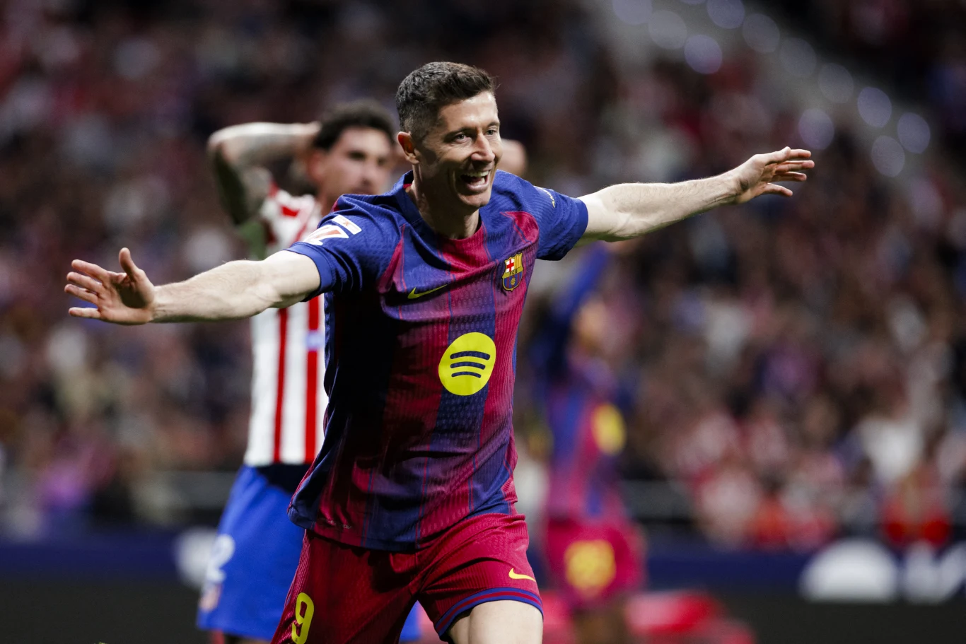 Robert Lewandowski Piłkarz w stroju Barcelony z uniesionymi ramionami w geście radości po zdobyciu gola podczas meczu na stadionie piłkarskim.