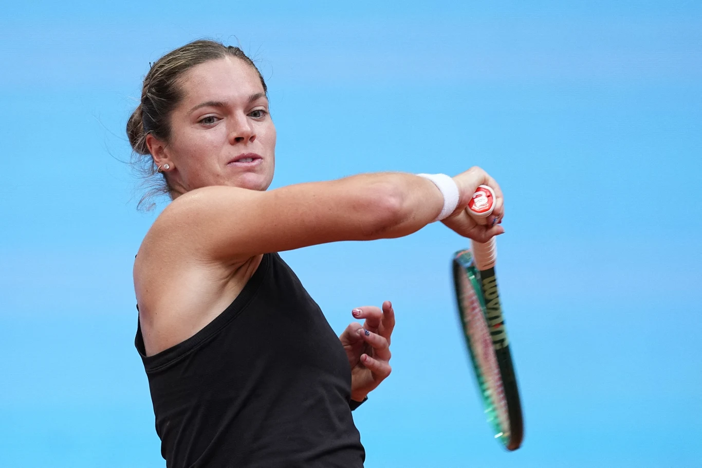 Kobieta w sportowej koszulce odbija piłkę tenisową rakietą na tle nieba.