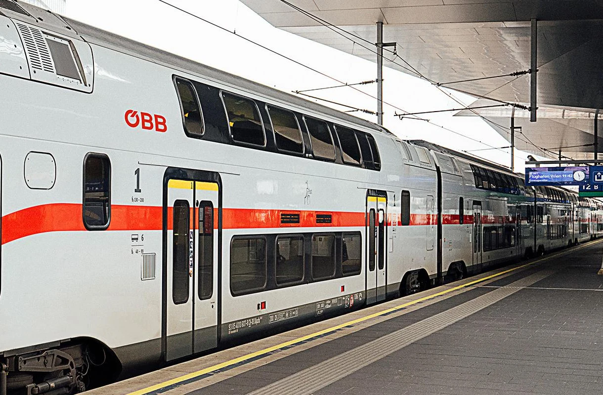Używane wagony piętrowe z Austrii na polskich torach. Kupi je PKP Intercity. Dwupoziomowy wagon pasażerski ÖBB przy peronie dużej stacji kolejowej z nowoczesną infrastrukturą.