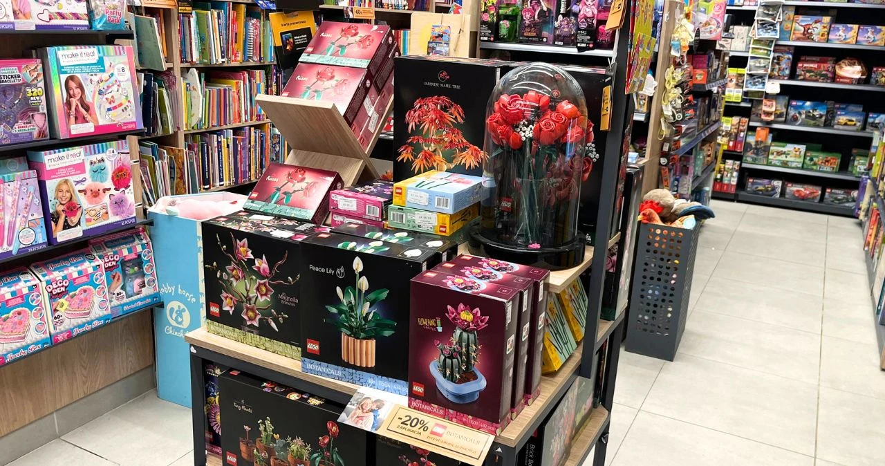LEGO kwiaty na Dzień Mamy. Gdzie kupić najpiękniejsze bukiety i zestawy taniej? Półka sklepowa z zestawami LEGO kwiaty i rośliny, obok kolorowe książki i czasopisma dla dzieci.