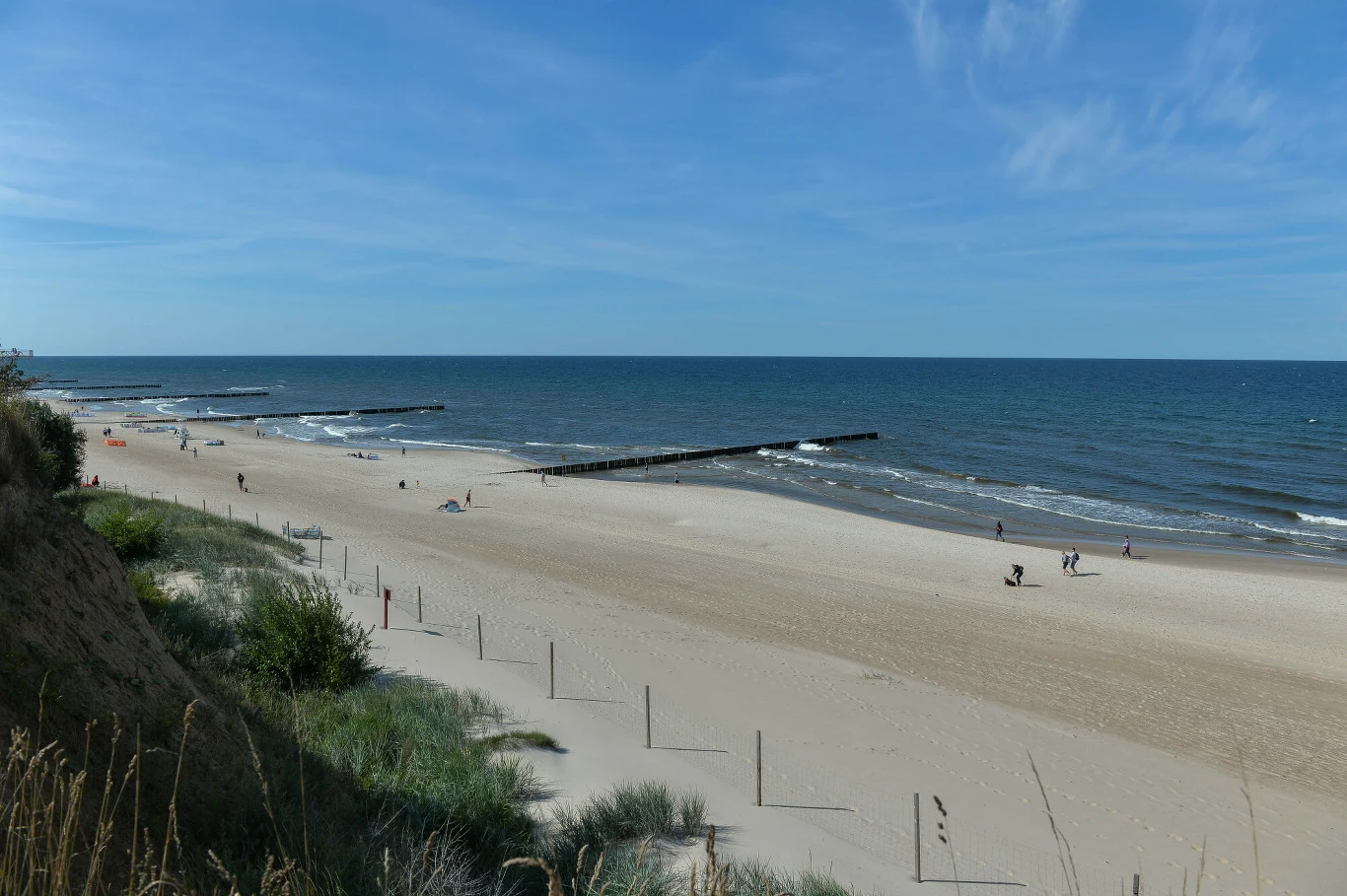 Pustkowo może pochwalić się piękną, szeroką plażą Szeroka, piaszczysta plaża z wydmami i kilkoma spacerującymi osobami, spokojne morze z niewielkimi falami oraz drewniane falochrony sięgające w głąb wody.