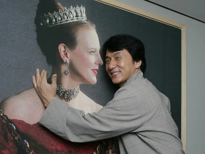 Jackie Chan z portretem królowej Małgorzaty II noszącej choker Uśmiechnięty mężczyzna w jasnym stroju obejmuje dużą, elegancką fotografię kobiety w koronie i ozdobnej sukni.