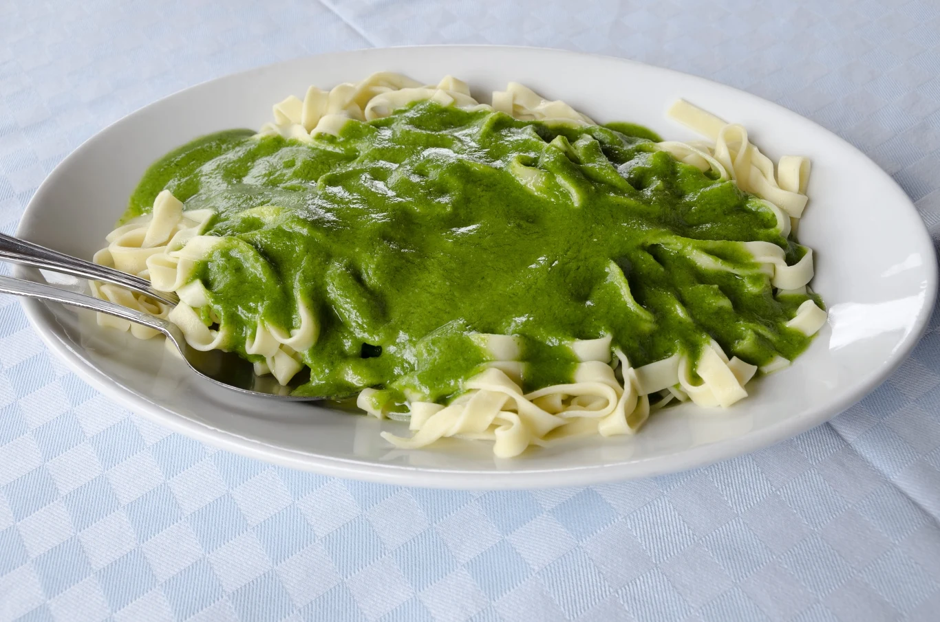 Szybki makaron dla leniwych Porcja makaronu tagliatelle polana aksamitnym zielonym sosem, podana na białym talerzu.