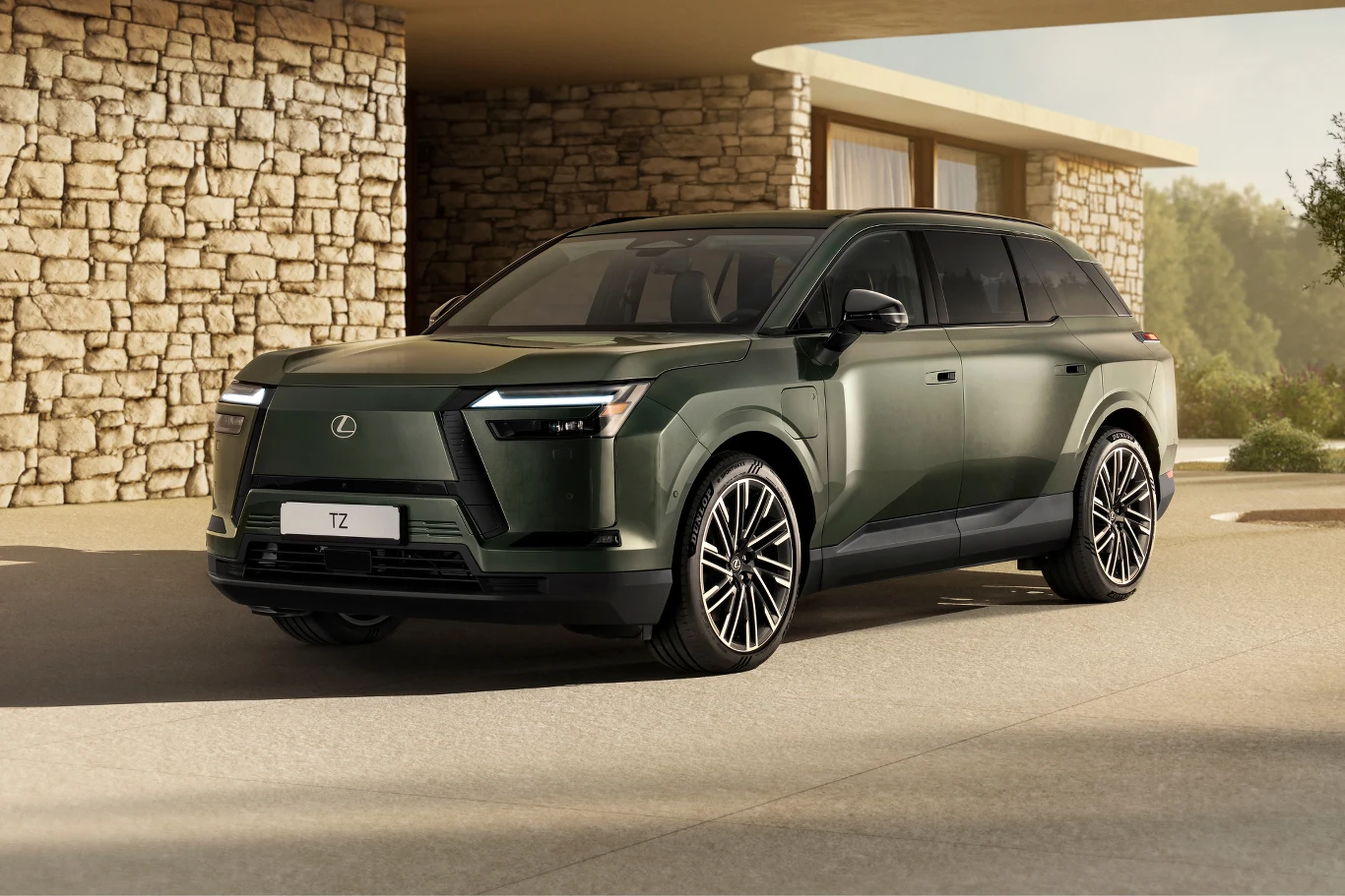 Nowoczesny SUV marki Lexus w odcieniu zielonym, ustawiony przed budynkiem o kamiennej elewacji, wyróżniający się dynamiczną sylwetką, masywnymi nadkolami i charakterystycznymi reflektorami w kształcie litery L.