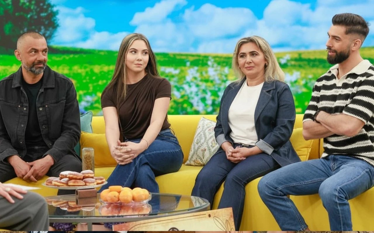 Cztery osoby siedzą na żółtej kanapie, patrząc w stronę rozmówcy; na stoliku przed nimi leżą pączki i płyta z wypiekami, a w tle widoczny jest ekran z wiosennym krajobrazem.