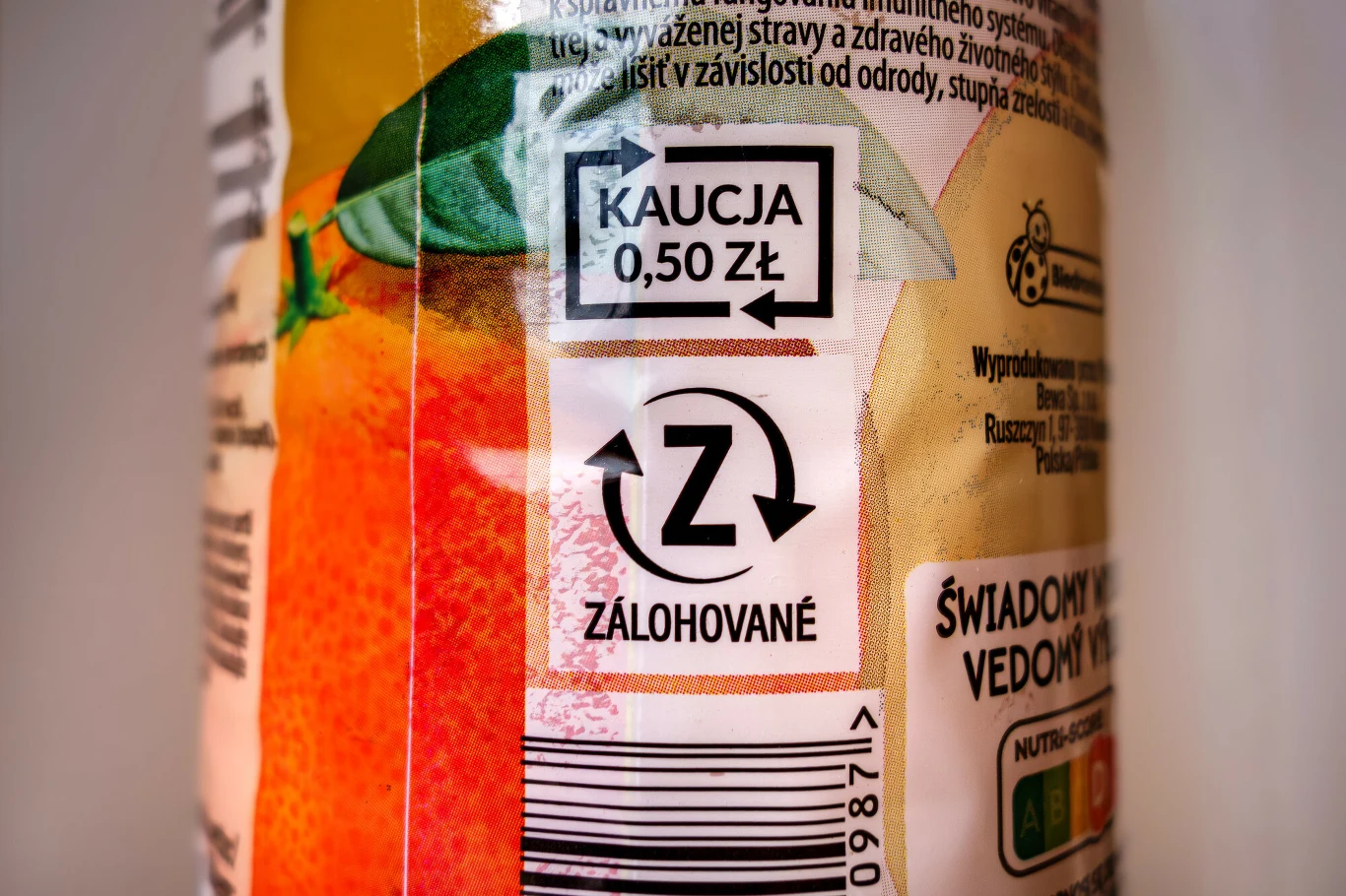 System kaucyjny działa w Polsce od 1 października 2025 r. Etykieta z napisem „Kaucja 0,50 zł”, logotypem z literą Z wskazującą produkt objęty systemem kaucyjnym, fragmentem kodu kreskowego oraz częścią owocu pomarańczy i zielonym liściem.