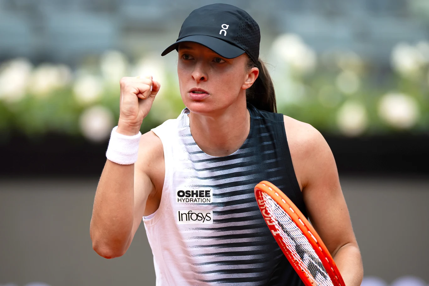 Tenisistka w sportowym stroju i czapce z daszkiem, z zaciśniętą pięścią w geście triumfu, trzymająca rakietę tenisową.