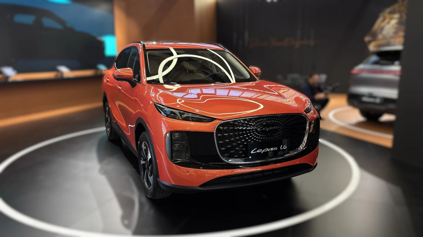 Czerwony SUV klasy premium z masywnym grillem, charakterystycznymi reflektorami i aerodynamiczną sylwetką ustawiony w jasnym świetle ekspozycyjnym na tle czarnego, nowoczesnego stoiska motoryzacyjnego.
