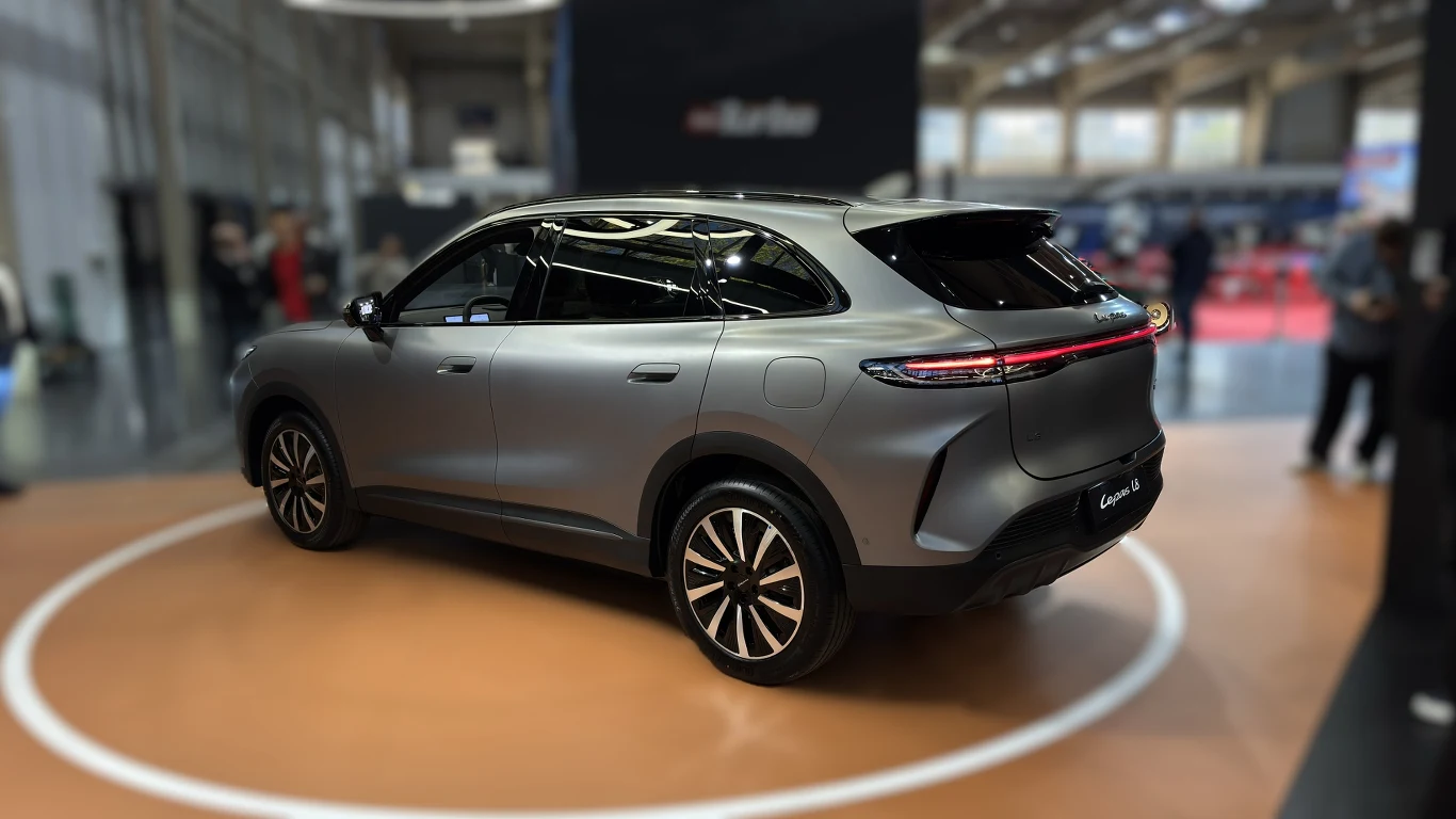 Nowoczesny, srebrny SUV o dynamicznej sylwetce i futurystycznych tylnych światłach LED, ustawiony na obrzeżach targów motoryzacyjnych.