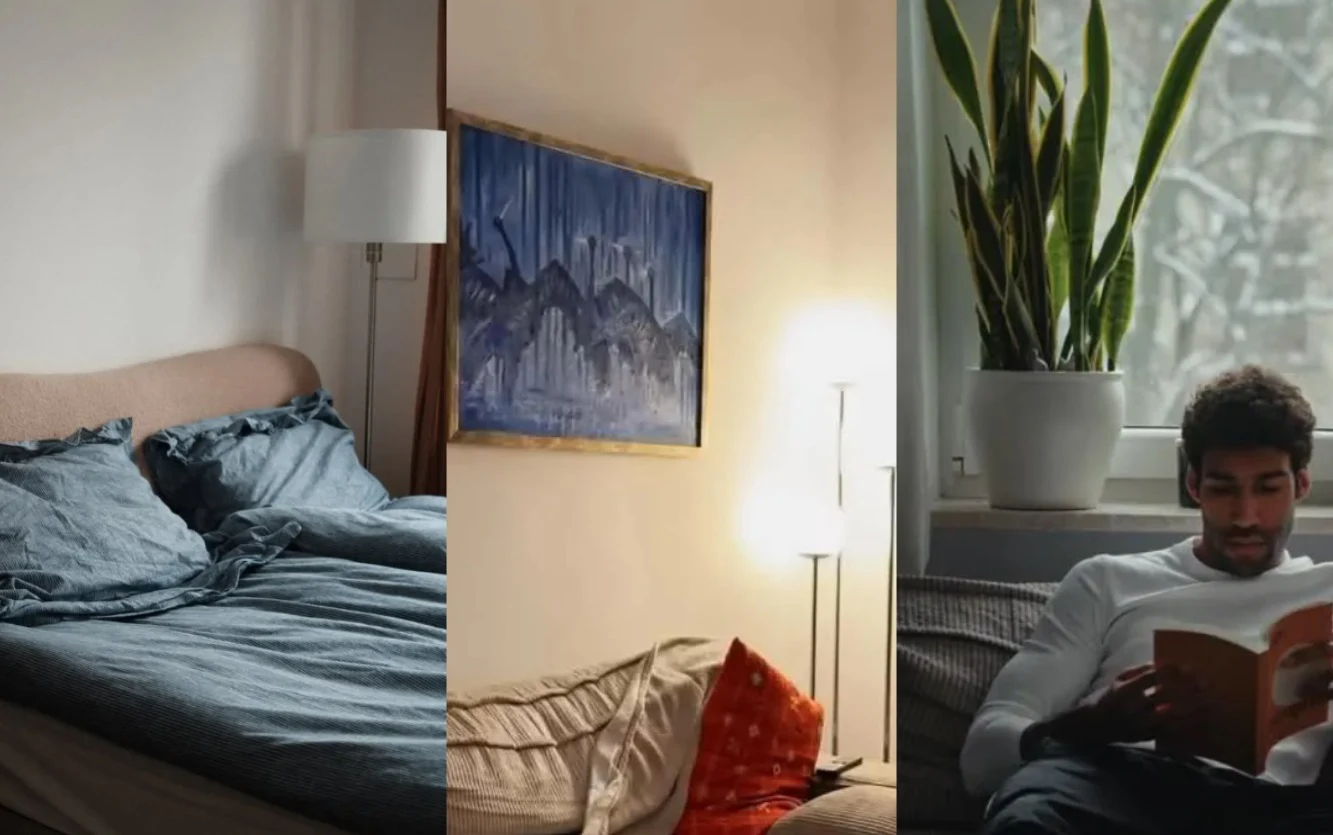 Łóżko z szarą pościelą oraz poduszkami, obraz w niebieskich odcieniach zawieszony nad sofą z lampą obok, mężczyzna siedzący przy oknie z dużą zieloną rośliną i czytający książkę.