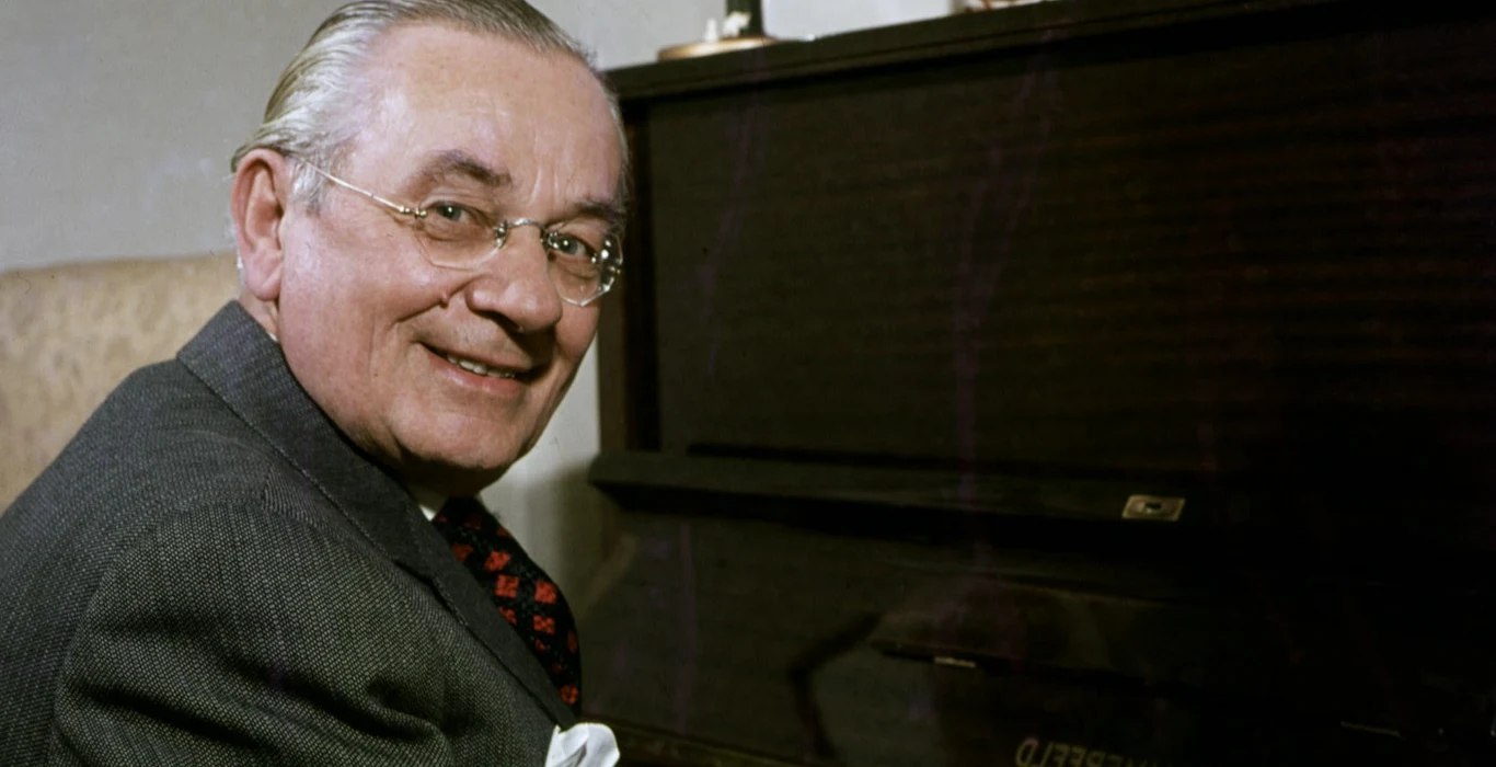 Mieczysław Fogg Mieczysław Fogg w okularach i garniturze siedzi przy pianinie, zwrócony w stronę aparatu.
