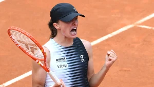 Zawodniczka tenisowa w czapce i sportowym stroju świętuje zdobycie punktu, trzymając rakietę i zaciśniętą pięść na kortach ziemnych.