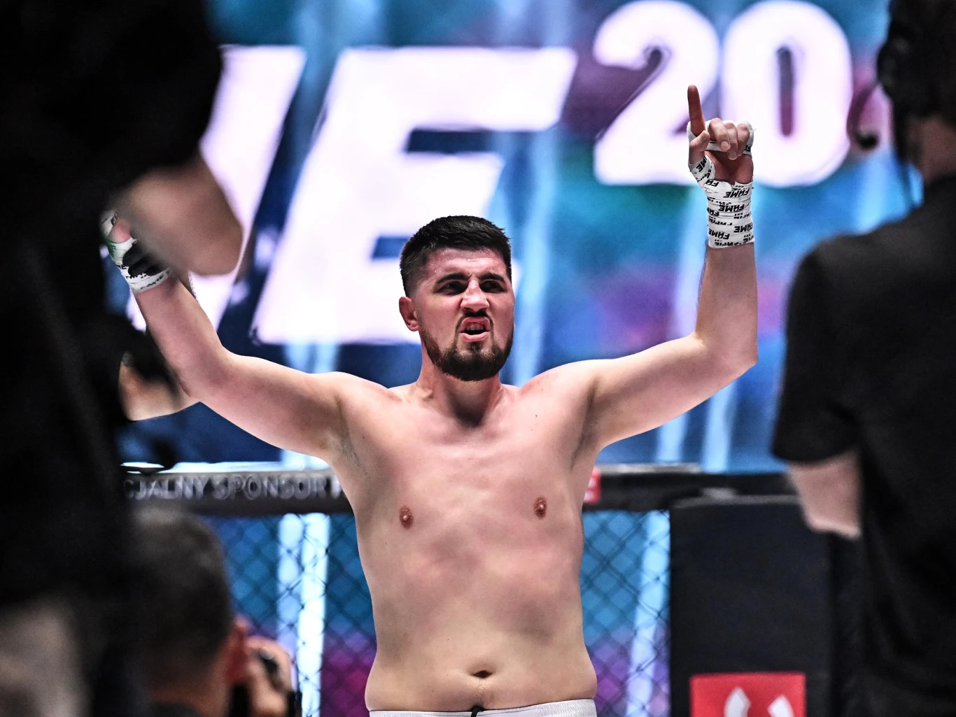 Zawodnik MMA z podniesionymi rękami w geście triumfu stoi na ringu po zakończonej walce, z widocznym wyrazem determinacji na twarzy.