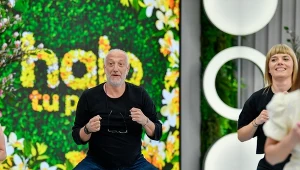 Grupa osób wykonująca wspólne ćwiczenia w jasnym, nowoczesnym wnętrzu z dekoracyjną, kwiatową ścianą i napisem 'halo tu' w tle.