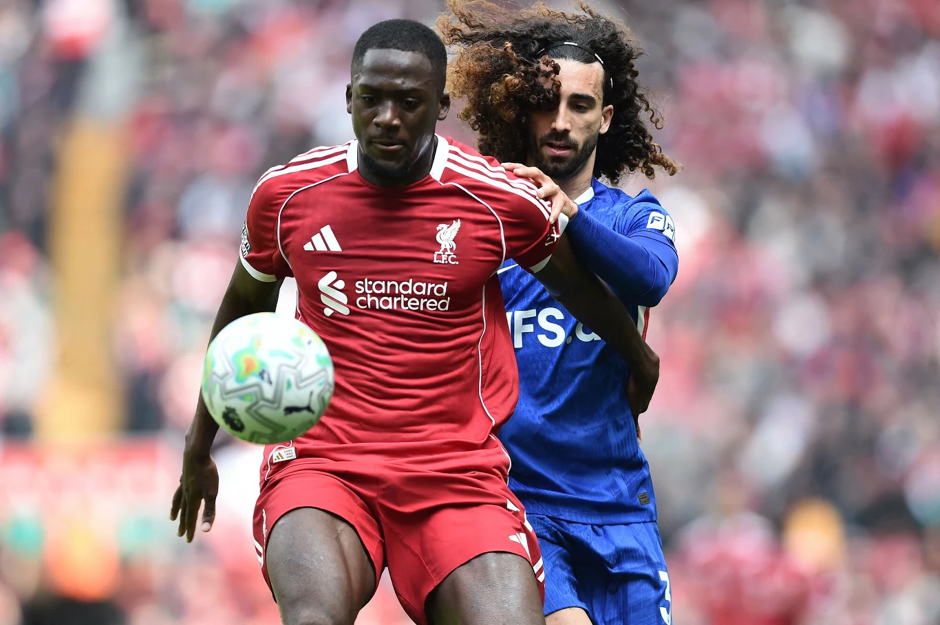 Dwóch piłkarzy walczy o piłkę, zawodnik Liverpoolu w czerwonym stroju jest z przodu, tuż za nim gracz Chelsea w niebieskim stroju próbuje go powstrzymać.