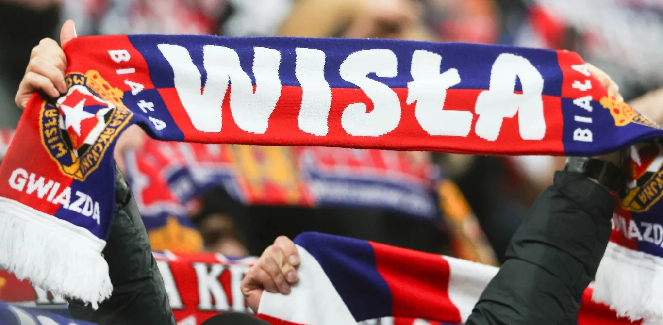 Wisła Kraków Szalik Wisły Kraków z napisem „WISŁA” i gwiazdą, trzymany przez kibiców, widoczne logo klubu i inne szaliki.