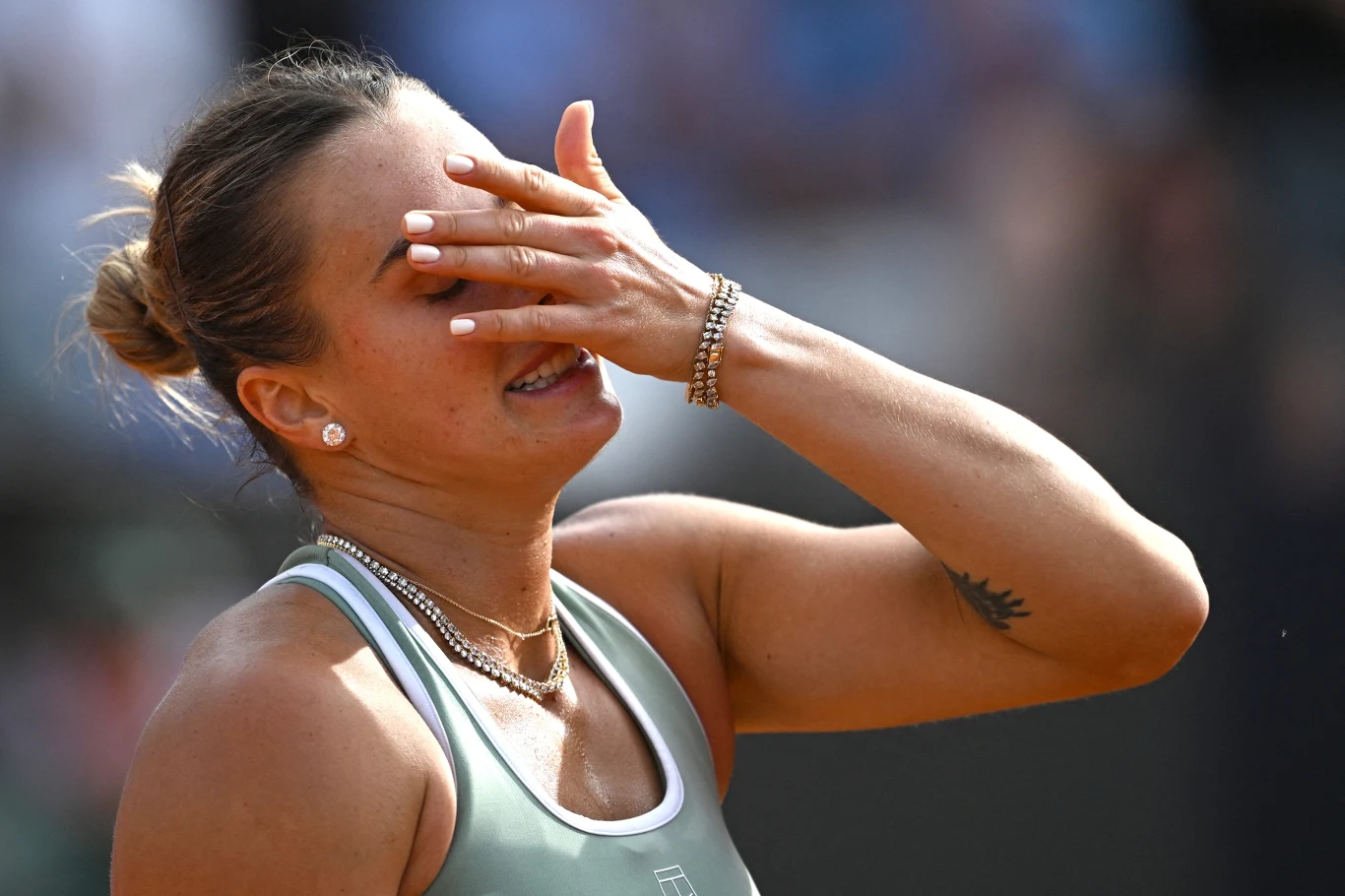 Tenisistka w sportowym stroju zakrywa twarz dłonią, wyrażając emocje podczas meczu.