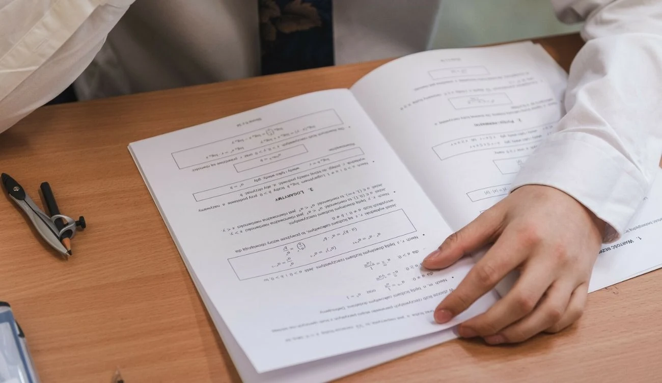 O godzinie 9:00 rozpoczęła się matura 2026 z matematyki rozszerzonej Otwarte materiały matematyczne z widocznymi wzorami i równaniami, dłoń osoby, cyrkiel na biurku.