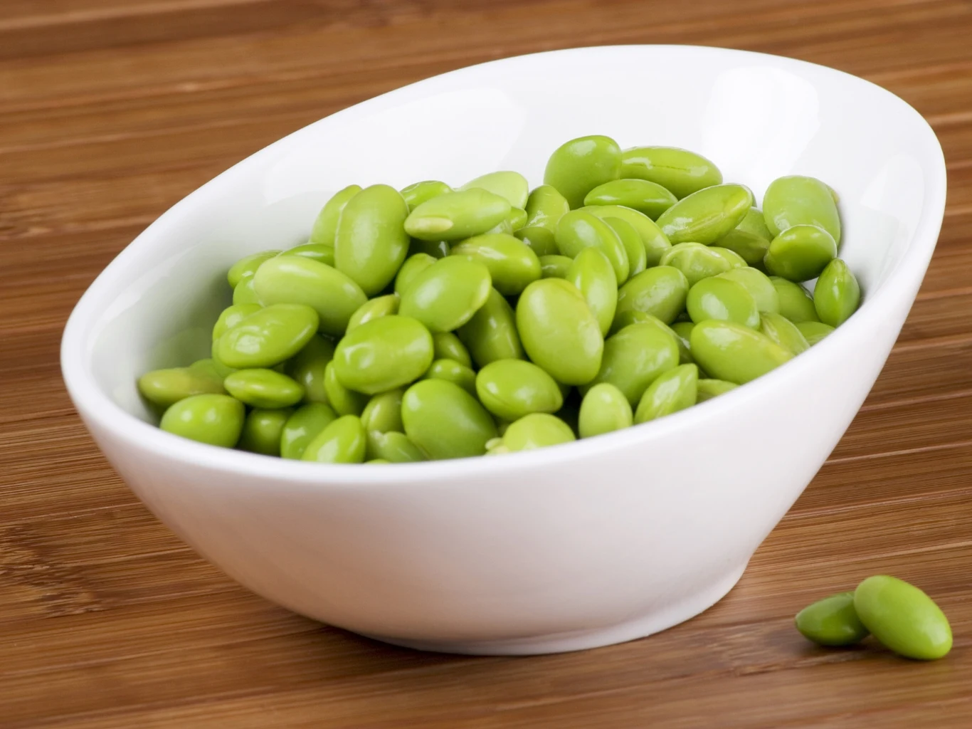 Fasola edamame może zastąpić produkty mięsne w diecie, bo zawiera dużo białka. Porcja zielonej fasoli edamame w białej miseczce na drewnianym blacie.