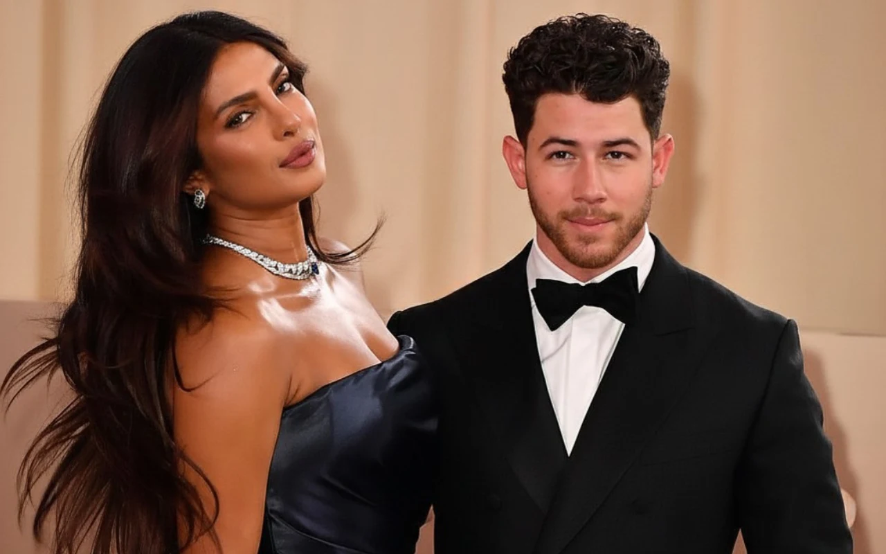 Priyanka Chopra i Nick Jonas Elegancka kobieta w granatowej sukni i naszyjniku z diamentami stoi obok mężczyzny w czarnym smokingu z muszką, oboje patrzą w stronę obiektywu.
