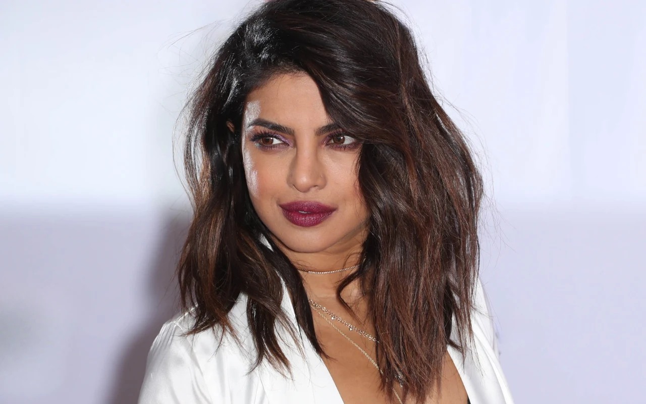 Priyanka Chopra to prawdziwa ikona Kobieta z ciemnymi, półdługimi włosami, ubrana w biały żakiet, z wyrazistym makijażem podkreślającym oczy i usta w kolorze bordowym, patrząca w bok na jasnym tle.