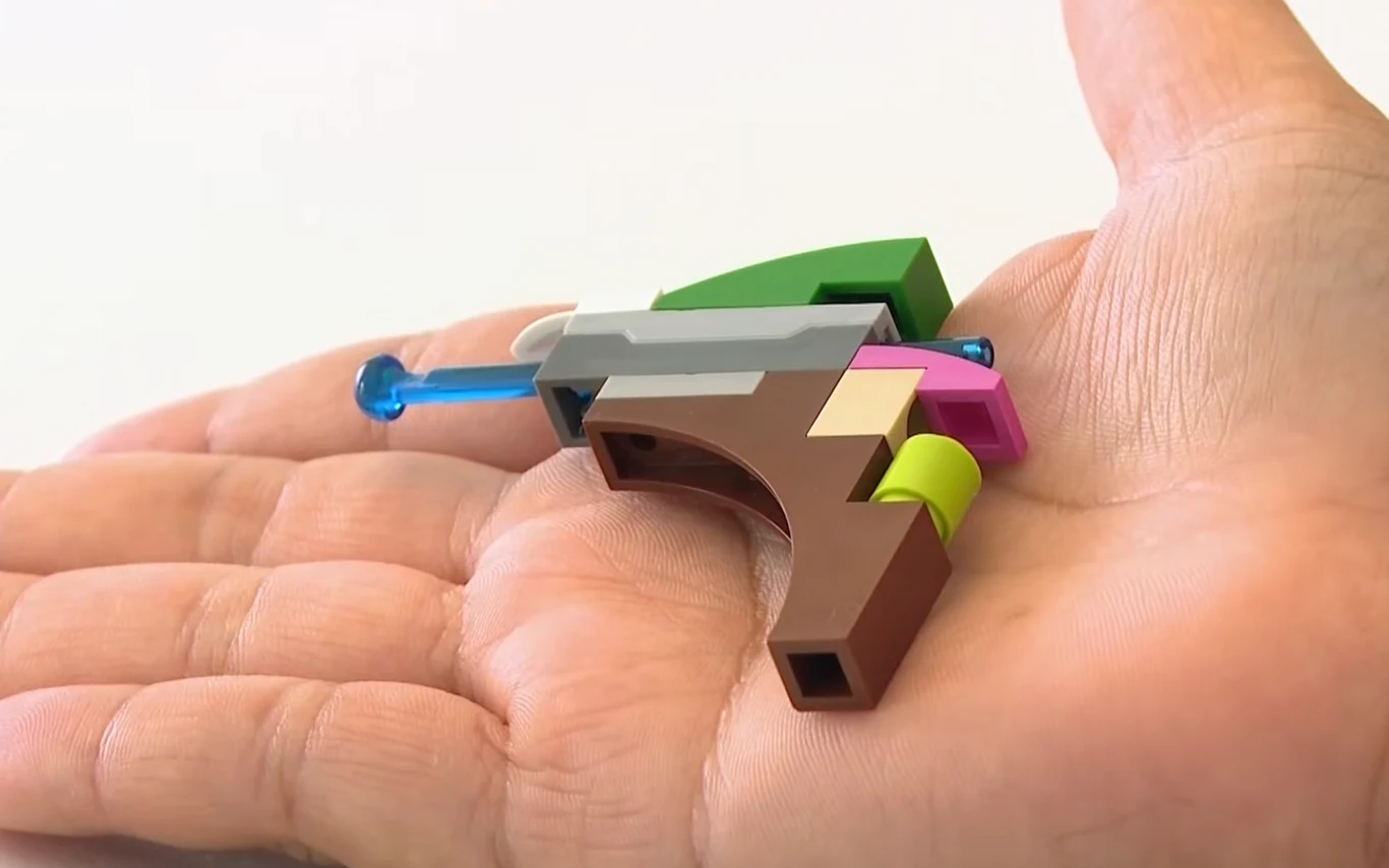 Miniaturowy pistolet z Lego Kolorowa konstrukcja z klocków Lego w kształcie miniaturowego pistoletu na otwartej dłoni.