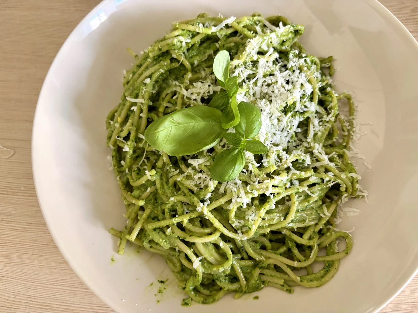 Spaghetti z zielonym pesto, posypane startym serem i udekorowane świeżą bazylią.